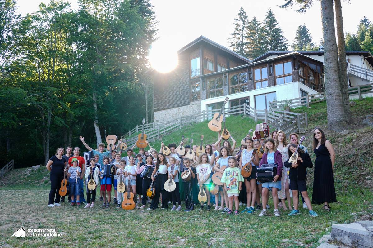 Stagiaires et équipe des Sommets de la Mandoline, instruments en main, devant le centre en montagne